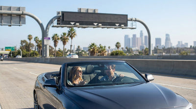 A car rental drives down a sunny Los Angeles freeway lined with palm trees