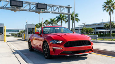 A modern car hire driving under a large green highway toll sign on a sunny day in Orlando