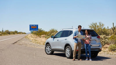 A car rental driving down a long, open highway through the Texas desert landscape towards the sunset