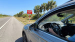 A red 'Wrong Way' sign seen from a car hire vehicle on a sunny Florida highway