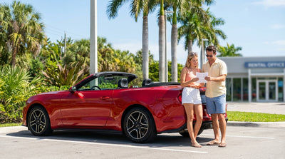 A convertible car hire driving down a sunny, palm-lined coastal road in Florida