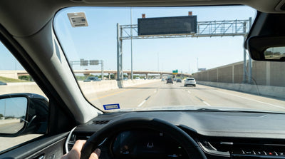 A silver car hire driving under an electronic toll gantry on a highway in Texas