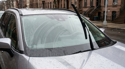 The driver's view from a car hire in New York as wipers smear rain across the windshield on a wet city street