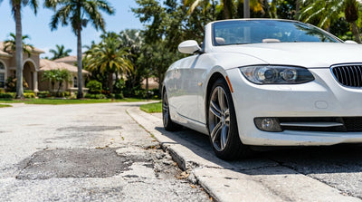 A close-up of a car rental wheel with scuff marks parked next to a cracked kerb on a sunny Florida street
