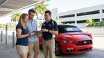 A bright red convertible car rental driving down a sunny street lined with palm trees in Miami