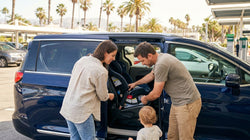 Parent securing a child into a safety seat in a car hire vehicle parked on a sunny Florida street