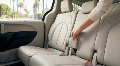 A parent fastens a child seat into the back of a family car rental on a sunny street in Los Angeles