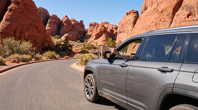A red convertible car hire on a scenic road winding through the striking sandstone formations of Red Rock Canyon near Las Vegas