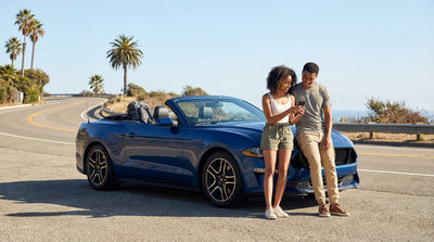 Young driver smiles in a convertible car hire on a sunny palm tree-lined street in Los Angeles