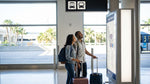A traveler with a suitcase waits for a car rental shuttle bus on the curb at LAX in Los Angeles