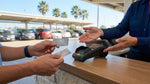A person handing a debit card to an agent at a car hire counter in a bright Texas airport terminal