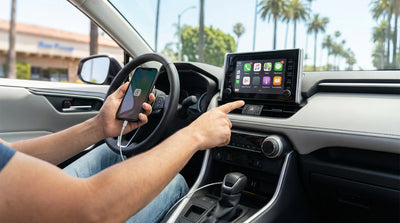 A driver connects a smartphone to the USB port of a car rental on a sunny street in Los Angeles