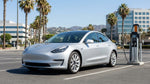 Modern electric car rental driving along a sunny street with tall palm trees in Los Angeles