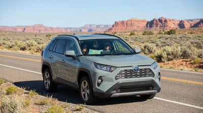A red car rental drives on an open desert highway away from the distant Las Vegas skyline at sunrise