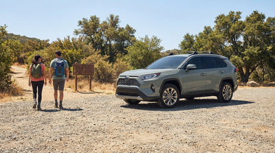 A silver car hire parked at a dusty trailhead in the California mountains with pine trees