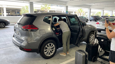 A parent installs a child car seat in the back of an SUV at their Orlando car rental parking spot
