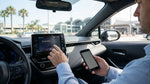 Driver pairing a smartphone to a car rental dashboard screen with Los Angeles streets visible outside