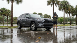 Silver car rental parked in deep flood water on a Florida street under stormy skies