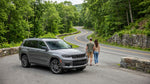 A white SUV car hire driving along a scenic, tree-lined parkway in New York on a bright sunny day