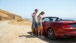 Driver looking under the hood of a car rental stopped on the side of a sunny California road
