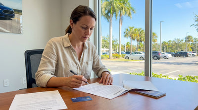 A person reviews a car hire agreement while standing next to a convertible on a sunny Florida road