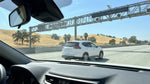 A car rental drives under a cashless electronic toll gantry on a sunny multi-lane highway in California