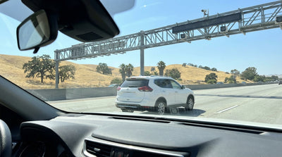 A car rental drives under a cashless electronic toll gantry on a sunny multi-lane highway in California