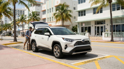 A driver unloads suitcases from a white car rental in a loading zone on a sunny Miami street with palm trees