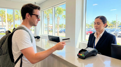 A person hands a credit card to an agent at a car hire desk in a bright Florida airport