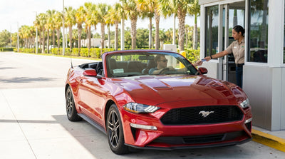 A white SUV car rental driving on a highway lined with tall palm trees on a sunny day in Florida