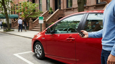 A blue Zipcar ready for car rental parked on a street in front of New York City brownstones