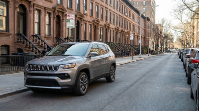 A silver car hire is parallel parked on a New York street with an alternate side parking sign in the foreground