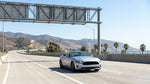 A silver car rental driving under a FasTrak toll plaza sign on a sunny California highway