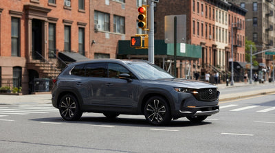 A car rental stopped at a red traffic light on a busy street corner in New York City