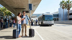 Travelers with luggage waiting for a car hire shuttle bus outside Terminal 6 at LAX in Los Angeles