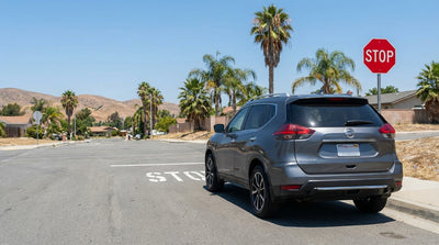 A modern car rental stopped at a four-way intersection on a sunny, palm-lined street in California