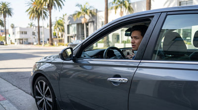 A person inspects the back of their white car hire in a sunny Los Angeles parking lot