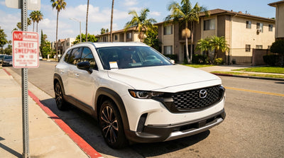 A modern car hire parked on a palm tree-lined street in Los Angeles next to a street sweeping parking sign