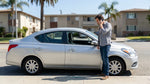 A white car rental with a shattered side window parked on a sunny street in Los Angeles