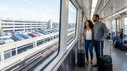 Passengers with suitcases exiting a JFK AirTrain in New York under a sign pointing to the car rental center