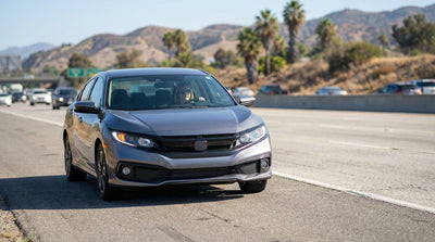 A car hire is stopped on the shoulder of a busy multi-lane freeway in Los Angeles under a clear, sunny sky