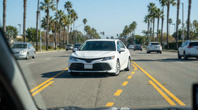 A car rental in the center turn lane of a busy California road, preparing to merge with traffic