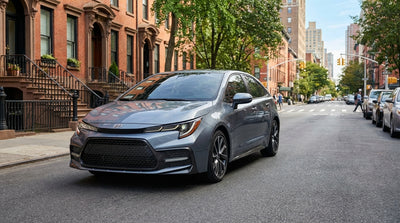 A red car hire drives across the Brooklyn Bridge toward the iconic New York City skyline on a sunny day