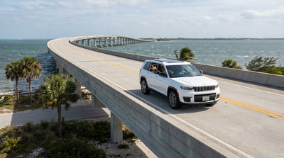 A car hire drives across a high, scenic bridge in Florida with white-capped waves on the ocean below