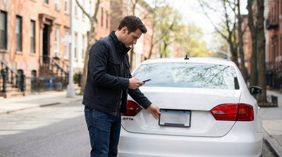 A person using a smartphone next to their parked car hire on a bustling street in New York City