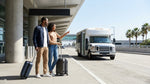 Travelers with luggage waiting for a car rental shuttle outside Terminal 1 at LAX in Los Angeles