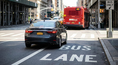 A car hire drives in a red bus-only lane on a busy street in New York City next to yellow taxis