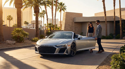 A sleek Audi R8 car rental parked on the Las Vegas Strip at night with vibrant casino lights reflecting on its exterior