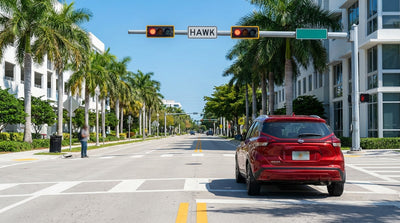 A car hire stopped at a crosswalk with a flashing HAWK beacon on a sunny, palm-lined street in Miami