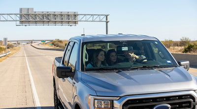 A sedan car rental driving under a large toll gantry on a multi-lane highway in Texas